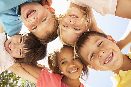 Kinder stehen im Kreis und blicken nach unten in die Kamera und lachen