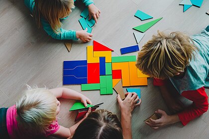 Kinder spielen mit bunten Holzplättchen auf dem Boden.